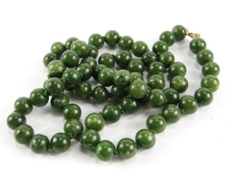 A string of sixty five jade beads, on a yellow metal clasp, stamped 9ct
