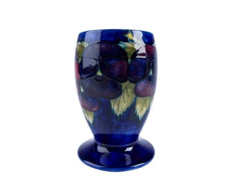 A Moorcroft vase featuring the classic Pansy pattern. This hand decorated piece showcases vibrant red and purple pansies with
