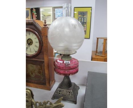 An Early XX Century Iron Based Oil Lamp, with twelve sided cranberry glass well and globular shade.
