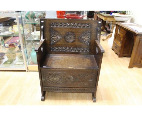 A Jacobean style oak Monks bench, with a carved back, carved front, raised on plinth feet 