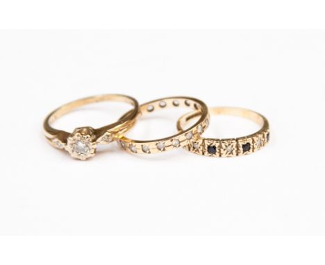 A diamond solitaire ring, a sapphire and diamond half hoop ring and an eternity ring set white stones.