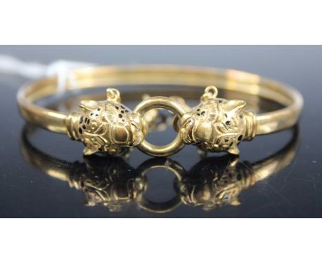 A yellow metal bangle, each end fashioned as an enamel set cheetah head, with safety chain, unmarked but tests as approx 9ct 