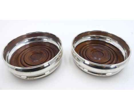 A pair of modern silver bottle coasters, each of squat circular form on a turned mahogany base, dia.14cmSmall dents and light