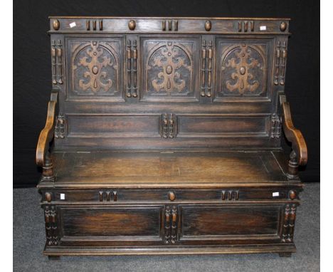 An early 20th century oak settle, the egg and dart rail over heraldic three panel back, downswept arms, box seat on block fee