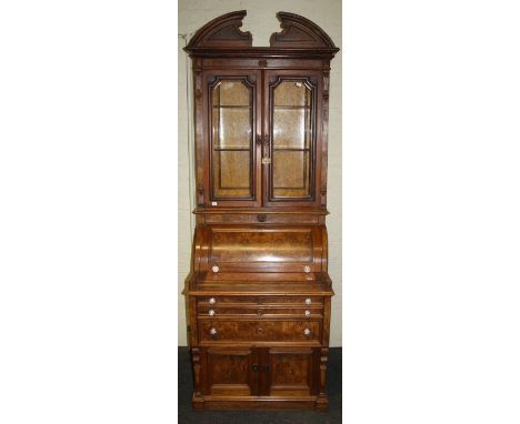 A late 19th century American walnut cylinder bureau bookcase, the broken arch pediment over glazed doors enclosing two shelve