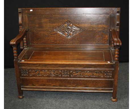 An early 20th century oak monks bench, the carved lozenge panel folding back over bobbin supported channeled arms, rising sea