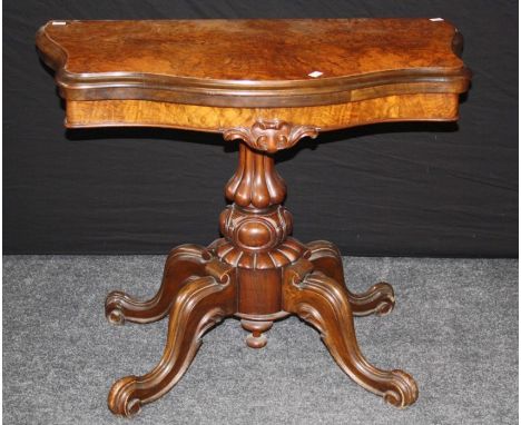 A Victorian figured walnut card table, the serpentine swivel folding top on lobed column, four downswept legs and scroll feet