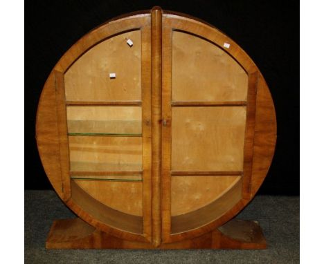 A 1930's walnut veneer 'moon' form display cabinet, the pair of glazed doors enclosing glass shelves, on a spreading plinth, 