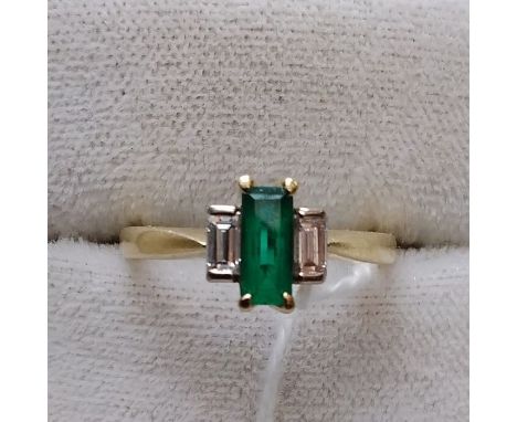 An 18ct emerald and diamond ring, claw set rectangular step cut emerald flanked by two bayonette cut diamonds. 3.4g. Total di