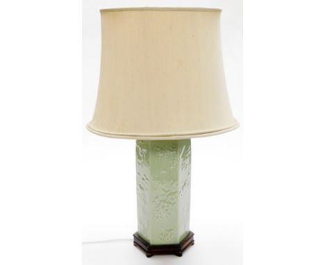 A Chinese hexagonal porcelain table lamp, the celadon sides with raised flower and leaf design, on a wooden base with cream s