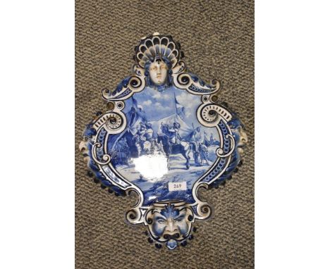 An early 20th Century blue and white Delftware wall plaque, of shield form, with hand painted scene to the centre, two sconce