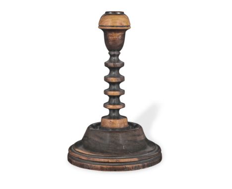 A 19th century turned lignum vitae taper stick, EnglishWith inverted acorn-shaped cup atop the blade-turned stem, on a spread