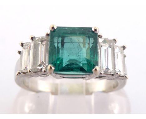 An emerald and diamond ring, the central rectangular emerald cut 6.9 x 6.8 x 5.2mm, claw set above tapering step set baguette