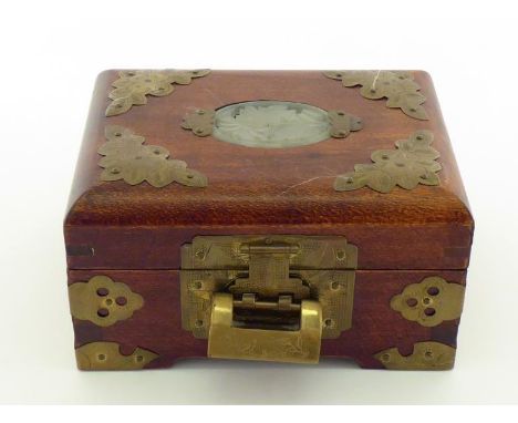 An oriental hardwood jewellery box with brass mounts, lock and key, the lid inset with a pierced oval jade plaque. 14x10x8cm.