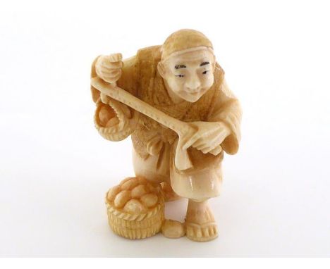 an ivory netsuke of a fruit merchant weighing his produce on a steelyard balance. Signed on the underside. 