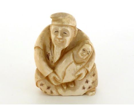 An ivory netsuke of an old man holding a baby wrapped in a shawl. Signed on the base. 