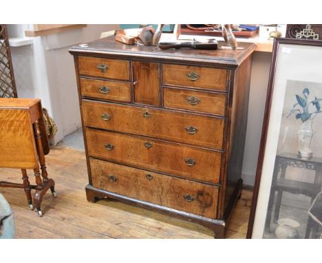 An early 18th century oak and walnut, boxwood-strung chest of drawers, the moulded rectangular top above a central cupboard d