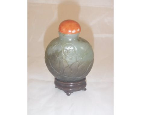 A Chinese carved hard stone snuff bottle decorated with figure upon a lotus flower with coral bead stopper, raised on a woode