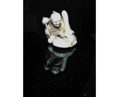 A Japanese Meiji period carved ivory netsuke as a mask maker, seated with a giant mask, bears inset signature to base, 3.5 cm