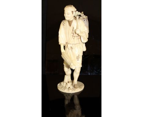 A Japanese Meiji Period carved ivory okimono as a man with parasol in one hand, a basket of vegetables over his shoulder, sig