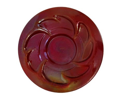 A Carter's Poole Pottery charger designed by Owen Carter, cast in relief and covered in a red lustre glaze incised Carter's P