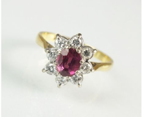 A ruby and diamond cluster ring, designed as a central oval mixed cut ruby claw set within a floral surround of eight brillia