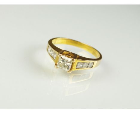 A Princess cut diamond ring, designed as a central Princess cut diamond claw set to tapering diamond set shoulders, the yello
