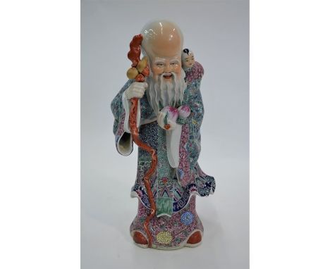 A Chinese Republic period famille rose figure of Shou Lao Fu, standing holding a long staff in his right hand, two peaches in