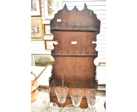 A 18th century artisan made vernacular spoon rack and utensil shelf in oak having shaped back with under drawer and shelf