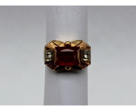 A ruby and paste set dress ring, the central rectangular ruby flanked by two white stones in a yellow metal setting and shank