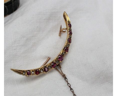 A ruby and diamond crescent shaped brooch set with nine round faceted rubies and ten diamonds to a yellow metal setting marke