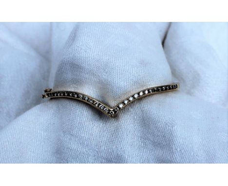 A yellow metal hinged bangle, set with thirty one round brilliant cut diamonds to a V setting, approximately 11.7 grams