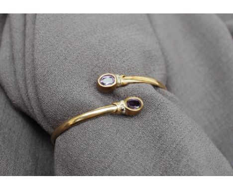 A 9ct yellow gold bangle, set with two oval faceted amethysts, approximately 7 grams CONDITION REPORT: Surface scratches and 
