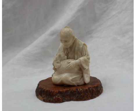 A late 19th century Japanese ivory figure depicting an elderly gentleman with glasses seated cross legged with a cat curled u