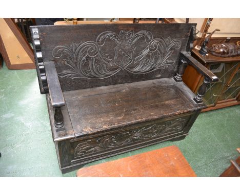 A dark oak monk's bench, the top carve with armorial cartouche and swags, hinged seat, lion mask cartouche to front panel.