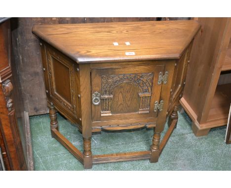 A Priory style side cabinet, oversailing top, canted front, arched panel door, turned supports.