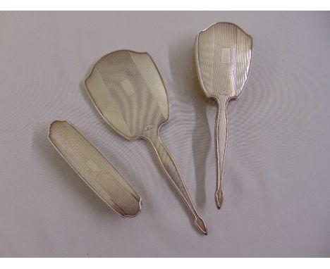 A silver engine turned dressing table hand mirror and two brushes