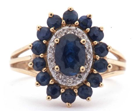 Modern sapphire and diamond cluster ring centring an oval shaped sapphire with a small sapphire surround, highlighted between