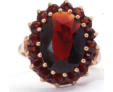 Garnet cluster dress ring, the large oval faceted garnet raised above small garnet surround, all in a basket setting, marks r