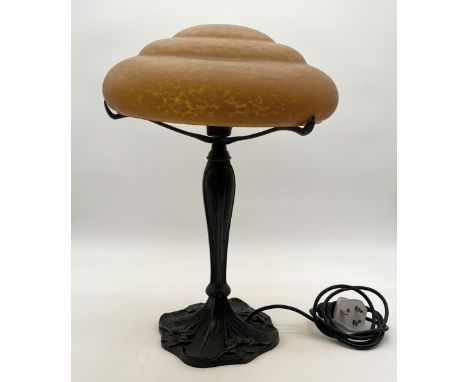 An Art Deco style lamp in the manner of Daum with cast metal base decorated in floral patterns and mottled amber domed shade