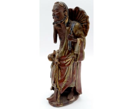 An Oriental figure of a sage with umbrella, wearing a cloak in sang de boeuf glaze. 23cm high, A/F