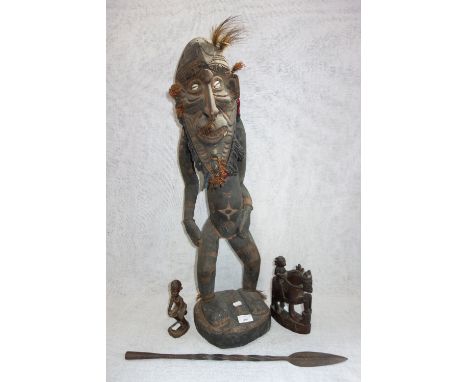 A LARGE CARVED WOODEN TRIBAL FIGURE, with cowrie shell eyes, 78 cm high, two similar carvings and an arrow 