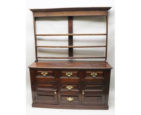 A GEORGE III OAK DRESSER BASE fitted three drawers across the top, above two small central drawers, flanked by panelled cupbo