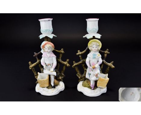 Pair of German Figural Candlesticks and Match Holders, a girl and a boy, each standing in front of a stylised tree trunk, whi