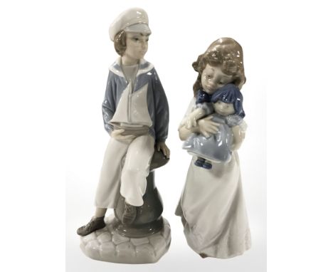 A Lladro figure modelled as a boy with a sailing boat, height 23.5 cm, together with a Nao figure of a child holding a doll.