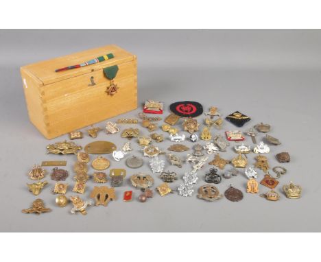 A hinged wooden box containing a very large collection of military badges, ribbons, brooches and medals. To include British A