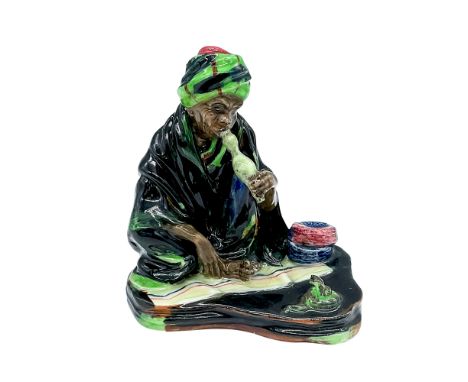 Glazed figure of a man playing the pungi to charming a snake. Royal Doulton backstamp.Issued: c. 1929-1938Dimensions: 4.5"L x
