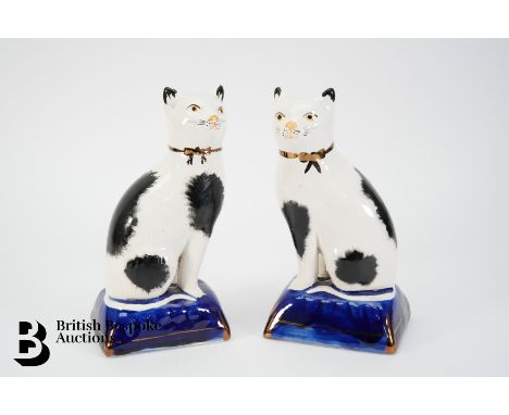 A pair of Staffordshire pottery cats, left and right facing, modelled seated, with black sponge patination, painted features 