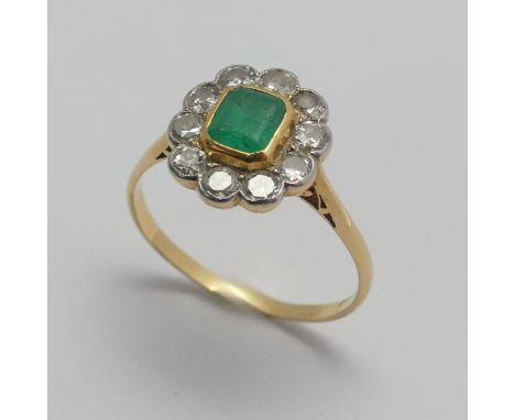 An emerald and diamond cluster Ring, the central emerald approx. 5x4.5mm collet set in yellow gold within a surround of ten s