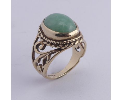 A jade Dress Ring, the oval cabochon stone approx. 13mm long, collet set in ropetwist mount with scrolling pierced shoulders,